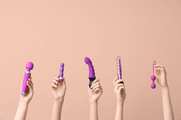 Женские руки с различными секс-игрушками на коричневом фоне