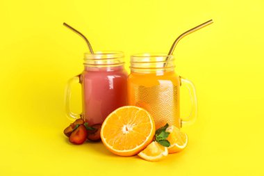 Sarı arka planda erik ve portakal suyu dolu Mason kavanozları.