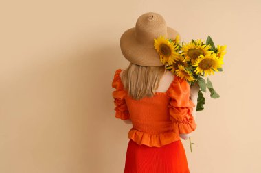 Hasır şapkalı, bej arka planda ayçiçekleri olan güzel bir kadın.