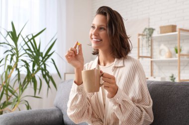 Evde bir fincan çay ve hapla güzel bir genç kadın.