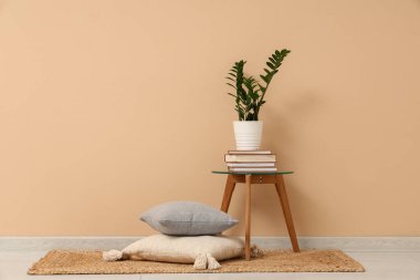 Bej duvarın yanındaki sehpada kitap ve bitki yığını var.