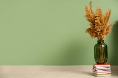 Yeşil duvarın yanındaki kitap yığınının üzerinde pampa otu olan vazo.