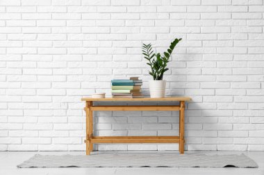 Beyaz tuğla duvarın yanındaki masada yığınla kitap ve bitki var.