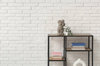 Beyaz tuğla duvarın yanında kitap ve dekor yığını olan raf ünitesi