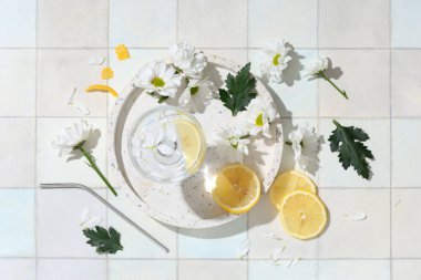 Bir bardak su, limon dilimleri ve arkaplanda papatya çiçekleri olan kompozisyon