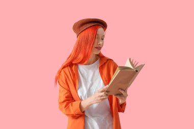 Bereli güzel, genç, mutlu bir kadın pembe arka planda kitap okuyor.