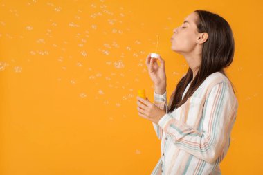 Sarı arka planda sabun köpüğü sallayan genç bir kadın.