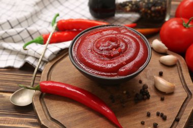 Bir kase kırmızı biber sosu ve ahşap arka planda farklı malzemeler.