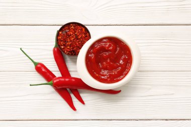 Taze biberli bir kase kırmızı biber ve beyaz ahşap arka planda pullar.