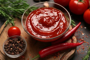 Bir kase kırmızı biber sosu ve siyah arka planda farklı malzemeler.