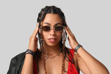 Gri arka planda rastaları olan şık, Afro-Amerikalı bir kadın.