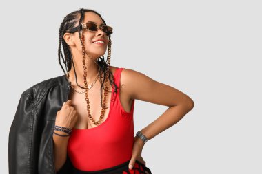 Gri arka planda rastaları olan şık, Afro-Amerikalı bir kadın.