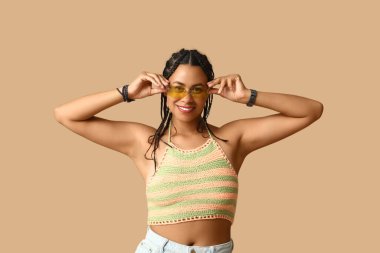 Kahverengi arka planda rastalı güneş gözlüklü güzel Afro-Amerikan kadın.