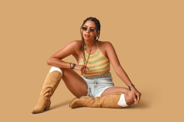 Güneş gözlüklü, kumral arka planda oturan güzel Afro-Amerikalı kadın.