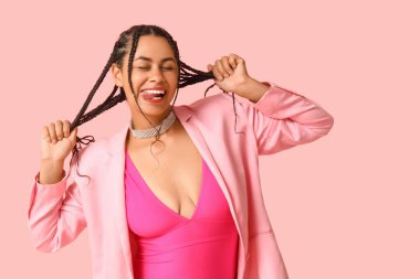 Pembe arka planda dilini gösteren rastalı Afro-Amerikan bir kadın.