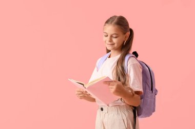 Sırt çantalı, pembe arka planda kitap okuyan tatlı bir kız öğrenci.