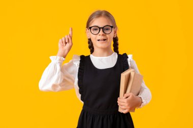 Kitapları sarı arka planda bir şeyi işaret eden sevimli liseli kız.