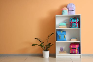 Turuncu duvarın yanında kitap ve sırt çantaları olan raf ünitesi.