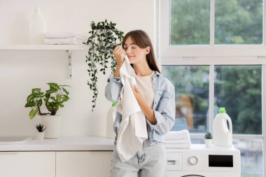 Çamaşır odasında temiz havlu kokusu alan genç bir kadın.