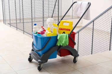 Temizlik malzemeleri ve ofisteki merdivenlerde uyarı levhası olan kapıcı vagonu.