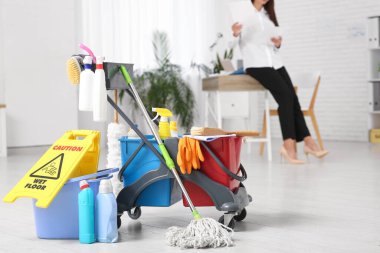 Ofiste hademenin tramvayında çalışan iş kadını, temizlik malzemeleri ve yerde uyarı levhası.