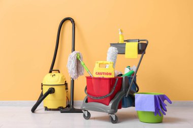 Temizlik malzemeleri ve elektrikli süpürgeyle sarı duvarın yanında temizlik arabası.