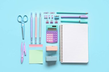 Mavi arkaplanda farklı kırtasiye malzemesi olan boş bir defter