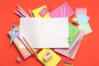 Kırmızı arkaplanda farklı kırtasiye malzemesi olan boş bir defter