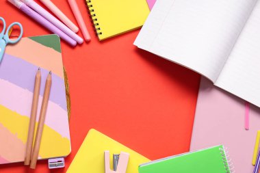 Kırmızı zemin üzerinde farklı kırtasiye malzemesi bulunan defterlerden yapılmış çerçeve