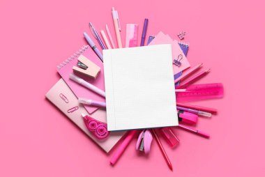 Pembe arka planda farklı kırtasiye malzemesi içeren boş bir defter