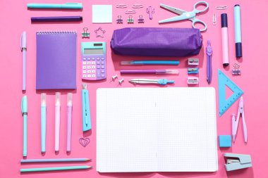Kalem kutusu ve pembe arkaplanda farklı kırtasiye malzemesi olan boş bir defter.
