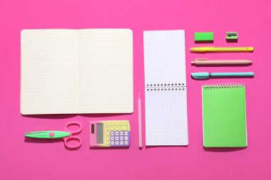 Pembe arka planda farklı kırtasiye malzemesi içeren boş defterler