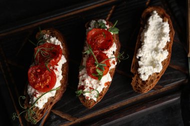 Siyah arka planda ricotta soslu lezzetli domates bruschetta tahtası.