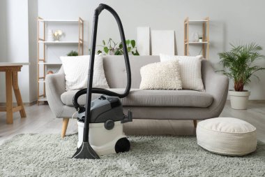 Evdeki gri kanepenin yanındaki halıda modern elektrikli süpürge.