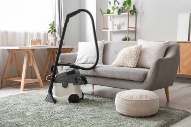 Evdeki gri kanepenin yanındaki halıda modern elektrikli süpürge.
