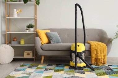 Oturma odasındaki gri kanepenin yanındaki halıda modern elektrikli süpürge.