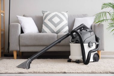 Oturma odasındaki gri kanepenin yanındaki halıda modern elektrikli süpürge.