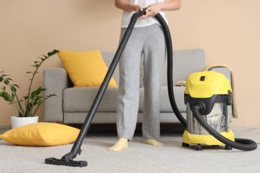 Kadın evinde elektrikli süpürgeyle halı temizliyor.