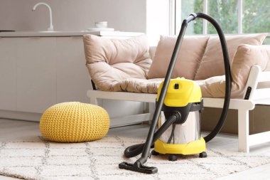 Evdeki beyaz kanepenin yanındaki halının üzerinde modern elektrikli süpürge.