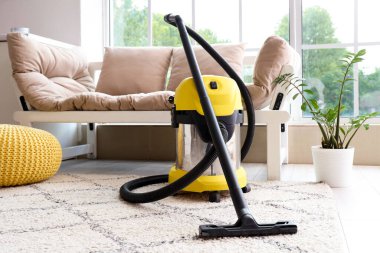 Evdeki beyaz kanepenin yanındaki halının üzerinde modern elektrikli süpürge.