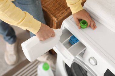 Delikanlı çamaşır makinesine çamaşır deterjanı dolduruyor.