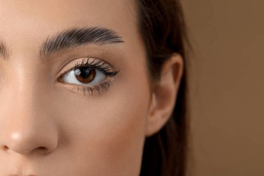 Kahverengi arka planda güzel kaşları olan genç bir kadın, yakın plan.