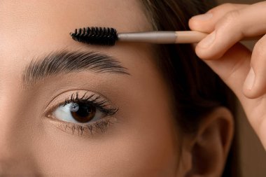 Kahverengi arka planda kaşlarının şeklini düzelten genç bir kadın, yakın plan.