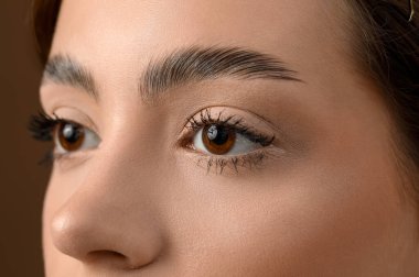 Kahverengi arka planda güzel kaşları olan genç bir kadın, yakın plan.