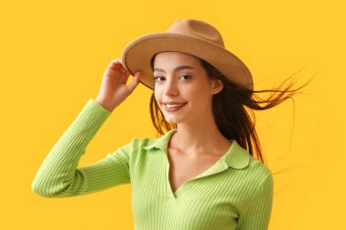 Sarı arka planda şık şapkalı güzel bir kadın.