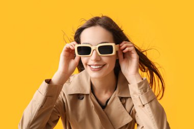 Sarı arka planda şık güneş gözlüklü güzel genç bayan.