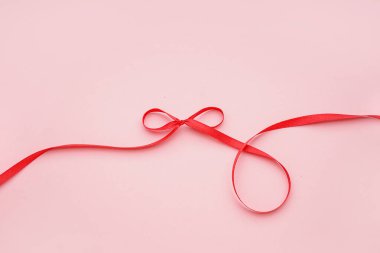 Pembe arkaplanda kırmızı kurdeleden yapılmış fiyonk
