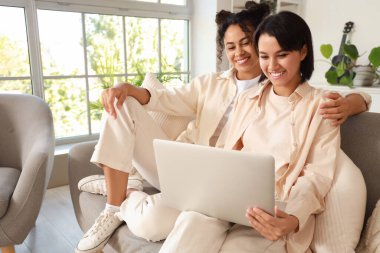 Evdeki kanepede dizüstü bilgisayar kullanan genç lezbiyen çift.