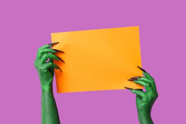 Mor arka planda turuncu kağıt çarşaflı cadının yeşil elleri. Cadılar Bayramı