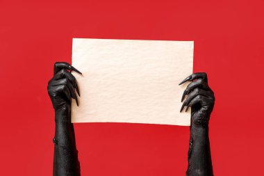 Kırmızı zemin üzerinde boş kağıt çarşaf ile cadının kara elleri. Cadılar Bayramı